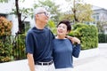 Happy retired senior Asian couple walking and looking at each other with romance in outdoor park and house in background.