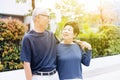 Happy retired senior Asian couple walking and looking at each other with romance in outdoor park and house in background.