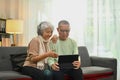 Happy retired spouses relaxing on sofa doing internet shopping and browsing internet in digital tablet Royalty Free Stock Photo