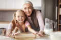 Happy retired woman in apron teaching little girl doing dough using rolling pin making cookies Royalty Free Stock Photo