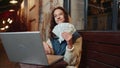 Happy rich girl using laptop winner victory holding fan of cash money in dollar banknotes in cafe