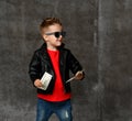 Happy rich kid boy millionaire in fashion sunglasses bundle a stack of money dollars cash in leather jacket