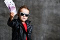 Happy rich kid boy millionaire in fashion sunglasses hold stack of 500 euro money cash in leather jacket and red t-shirt