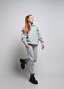 Happy slim red-haired woman with ponytail hairstyle in trendy grey sportswear hoodie, pants and black shoes walks, runs Royalty Free Stock Photo