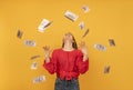 Happy rich young woman under money rain or throwing money around on orange background. Big profit or win lottery concept Royalty Free Stock Photo