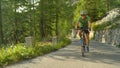 Happy road cyclist pedalling up an empty asphalt road in the lush green forest.