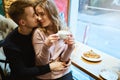 Happy romantic couple sitting over the window in cafe, embracing, kissing and drinking coffee. boyfriend tenderly Royalty Free Stock Photo