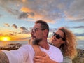 Happy and romantic couple of traveler take selfie picture with modern smartphone at the beach with amazing orange sunset in Royalty Free Stock Photo