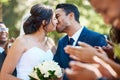Happy romantic newlywed couple kissing outside while surrounded by friends and family on their wedding day. Bride and Royalty Free Stock Photo