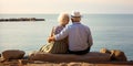 Happy romantic senior couple kissing sitting in front of the sea, two elderly people loving each other and enjoying beach vacation Royalty Free Stock Photo