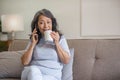 A happy 60s Asian woman enjoys her coffee and talking on the phone Royalty Free Stock Photo