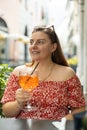 Happy 30s girl sitting on the cafe terrace on the city street. Woman hands toasting with aperol spritz cocktail. Concept Royalty Free Stock Photo