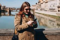 Happy 30s girl using smartphone on famous Old bridge in Florence. Stylish woman visiting Italian landmarks. Concept of Royalty Free Stock Photo