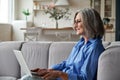 Happy 60s mature woman using laptop computer sitting on couch at home. Royalty Free Stock Photo