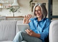 Happy 60s mature woman waving hand holding digital tablet video calling at home. Royalty Free Stock Photo