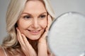 Happy 50s middle aged woman touching face skin looking in mirror. Royalty Free Stock Photo
