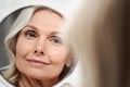 Happy 50s middle aged woman touching face skin looking in mirror reflection. Royalty Free Stock Photo