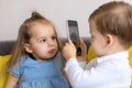 happy and sad little cute preschool siblings baby brother and child sister talk video conference on yellow gray sofa