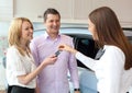 Happy saleswoman handing over car keys to attractive young family Royalty Free Stock Photo