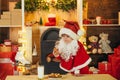 Happy Santa Claus - cute boy child eating a cookie and drinking glass of milk at home Christmas interior. Little Santa