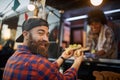 Happy, satisfied caucasian male with beard customer receiving sandwiches from a polite employee in fast food service, turning his