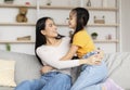 Happy satisfied chinese young female look at girl have fun, hugging, enjoying time together in living room