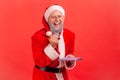 Happy satisfied elderly man with gray beard wearing santa claus costume holding paper notebook and Royalty Free Stock Photo