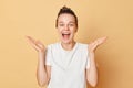 Happy satisfied woman wearing white T-shirt washes hair standing with shampoo foam on her head isolated over beige background