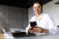 Happy satisfied young entrepreneur, business woman using mobile phone at home workplace, chatting, browsing internet, reading Royalty Free Stock Photo