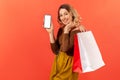 Happy satisfied young woman holding paper bags showing smartphone with white screen, mobile application for shopping online Royalty Free Stock Photo