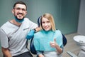 Happy satisfied young woman sit in char and smile. She hold big thumb up. Male dentist stand beside her and smile too