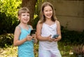 Happy school age kids two young girls children holding their smartphones mobile phones in hands outdoors, outside smiling. Using Royalty Free Stock Photo