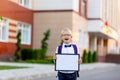 A happy schoolboy boy with blond glasses and a backpack stands at the school and holds a sign with a white sheet. Day of knowledge