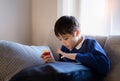 Happy schoolboy eating red apple while playing game online with friend on tablet,Kid using internet sending homework to the Royalty Free Stock Photo