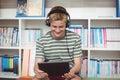 Happy schoolboy listening music while using digital tablet in library Royalty Free Stock Photo