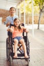 Happy schoolboy pushing a girl on wheelchair Royalty Free Stock Photo