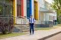 Happy schoolboy in white shirt, blue tie and backpack left school with multicolored windows Royalty Free Stock Photo