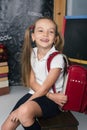 Happy schoolchild in the classroom with big backpack