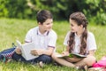 happy schoolchildren doing homework together while sitting on grass
