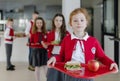 Happy schoolchildren in uniforms holding trays with lunch and standing in queue in school canteen. Royalty Free Stock Photo