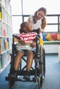 Happy schoolgirl carrying schoolboy in wheelchair Royalty Free Stock Photo