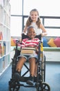 Happy schoolgirl carrying schoolboy in wheelchair Royalty Free Stock Photo