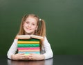 Happy schoolgirl with pile books near empty green chalkboard Royalty Free Stock Photo