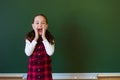 Happy schoolgirl preschool girl in plaid dress standing in class near a green blackboard. Concept of school education Royalty Free Stock Photo