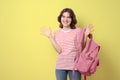 Happy schoolgirl smiling and holding backpack, looking at camera, on yellow background