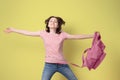 Happy schoolgirl smiling and jumping with pink backpack, looking at camera, on yellow background
