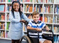 Happy schoolgirl standing with schoolboy on wheelchair Royalty Free Stock Photo