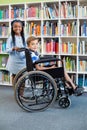 Happy schoolgirl standing with schoolboy on wheelchair Royalty Free Stock Photo