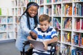 Happy schoolgirl standing with schoolboy on wheelchair using digital tablet Royalty Free Stock Photo