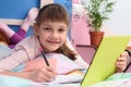 Happy schoolgirl studies remotely at home, lies in bed and joyfully looked into the frame